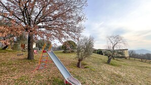 Un parque infantil con tobogán y columpios, rodeado de árboles y césped.