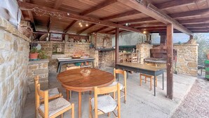 Un patio exterior con paredes de piedra, una mesa de madera y sillas, y un horno de piedra.