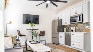 A modern kitchen with white cabinets, a microwave, and a dishwasher. There is a dining area with a table and chairs, and a ceiling fan above. - Sage at The Shire 255 - Unit A - Downtown! (Southern Pines)