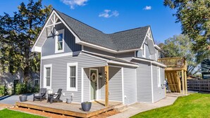 A two-story house with a grey exterior, a front porch with chairs, and a deck. - Sage at The Shire 255 - Unit A - Downtown! (Southern Pines)