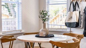 Een eethoek met een ronde tafel, houten stoelen, een vaas met planten en een raam met jaloezieën.