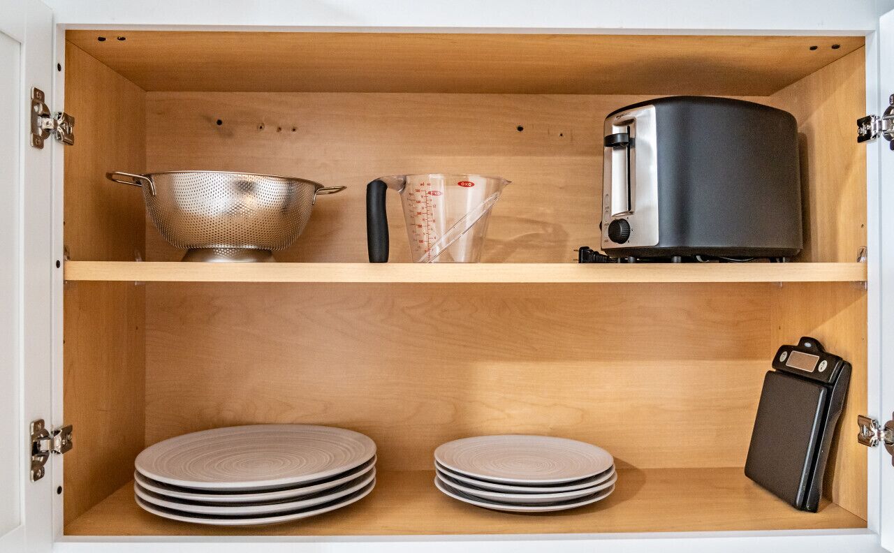 Un mueble de cocina con un colador de acero inoxidable, una taza medidora y una tetera eléctrica negra.