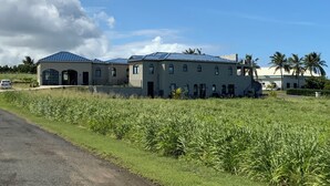 Un edificio grande de varios pisos con techo plano y ventanas arqueadas, rodeado por un campo cubierto de césped y palmeras.