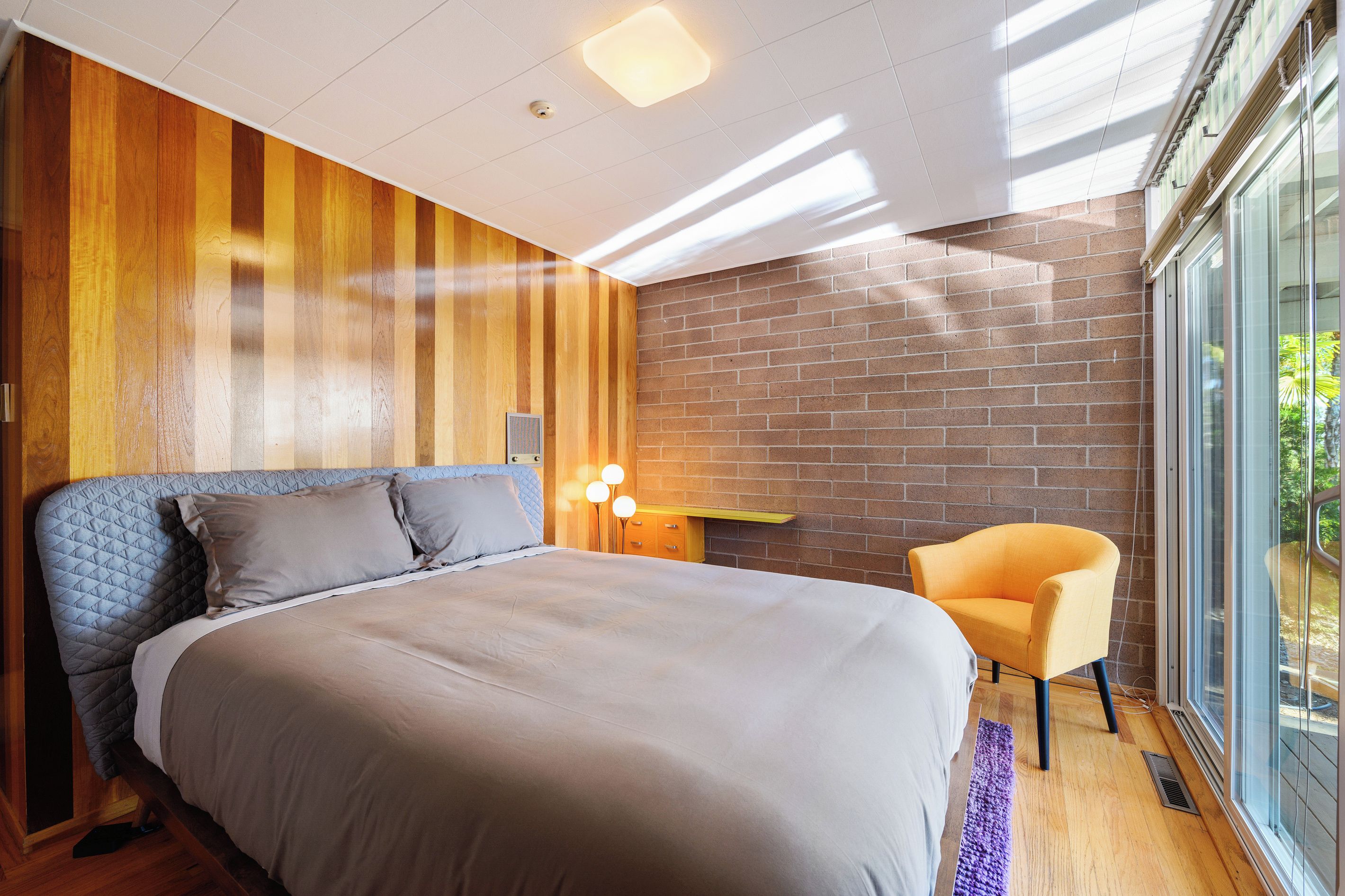A modern bedroom with a large bed, a chair, a desk, and a view through a large window.