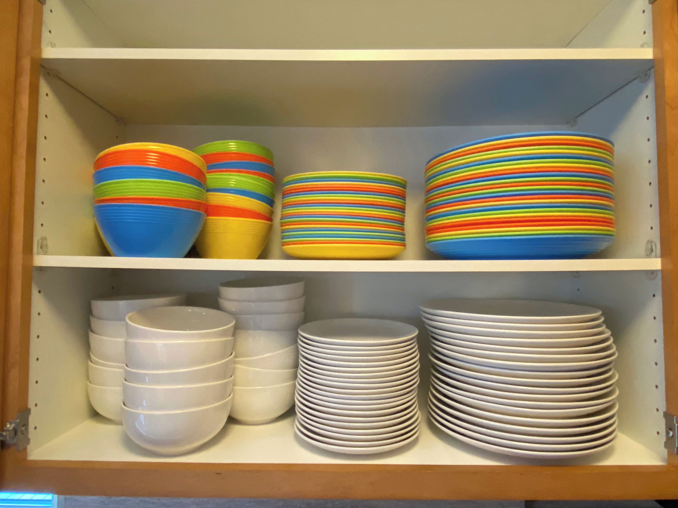 A cabinet with multiple shelves containing stacks of colorful and white bowls and plates.