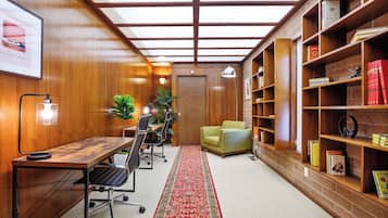 A room with a wooden desk, chairs, a bookshelf, and a red carpet.