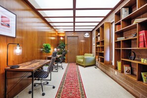 Een kamer met een houten bureau, stoelen, een boekenkast en een rood tapijt.