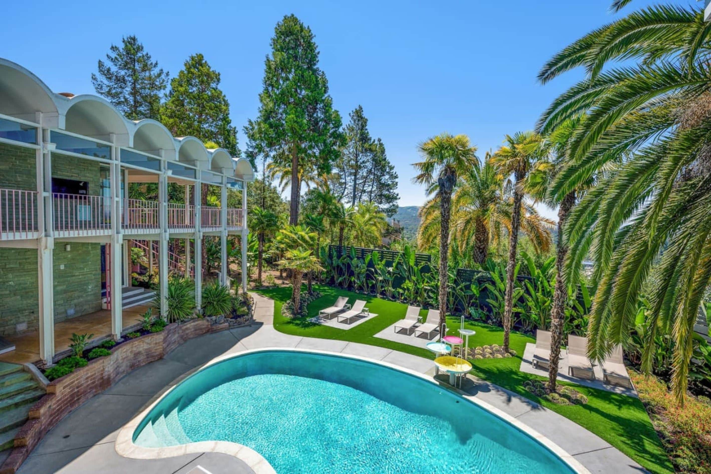 A swimming pool with a curved edge, surrounded by a well-maintained lawn and palm trees.