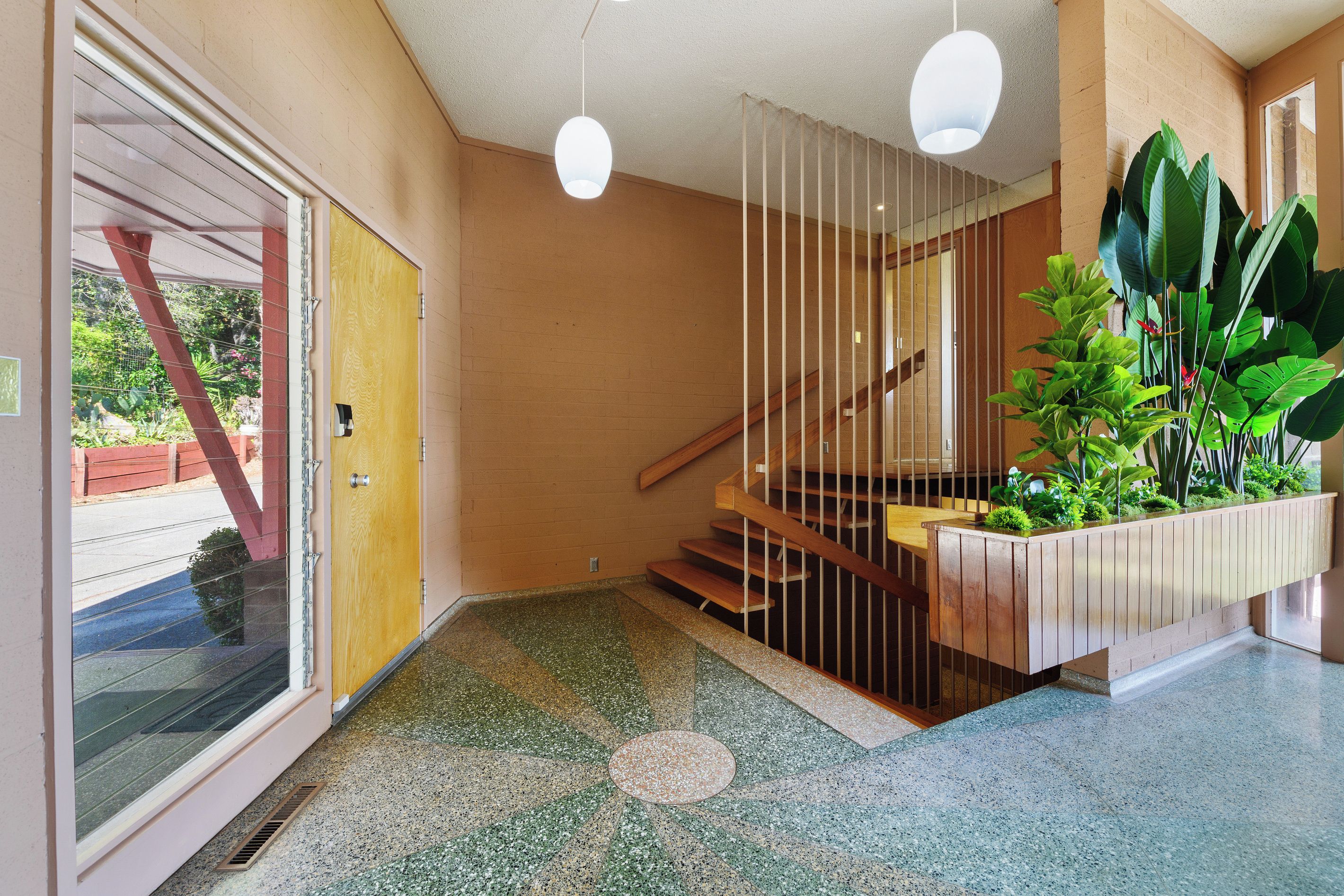 A modern interior with a wooden staircase, a glass door, and a plant arrangement.