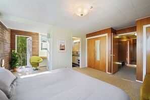 Een slaapkamer met een bed, een stoel, een plant in pot, een deur en uitzicht op een badkamer.