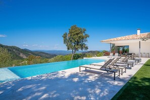 A modern outdoor pool area with lounge chairs, a clear view of the surrounding hills, and a building with a tiled roof. - 5 bedroom accommodation in La Garde-Freinet (La Garde-Freinet)