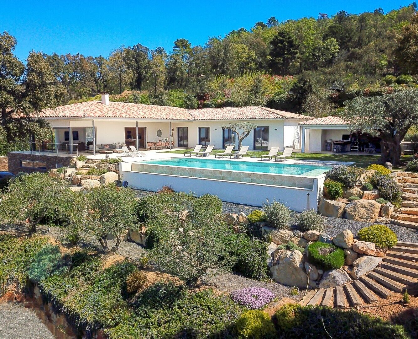 Une maison avec une piscine, entourée de jardins aménagés et d’arbres.