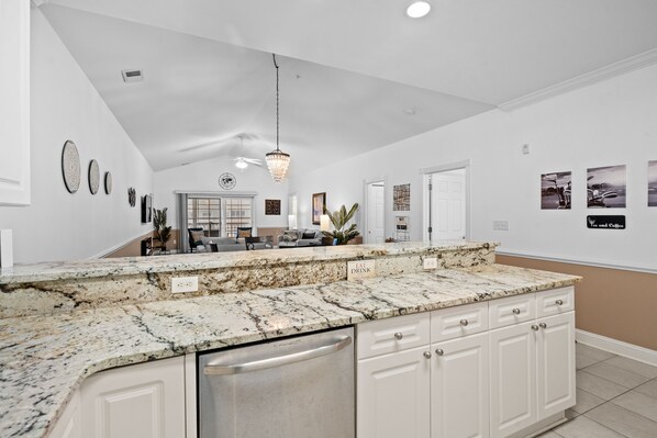 A kitchen with a granite countertop, white cabinets, and a dishwasher.