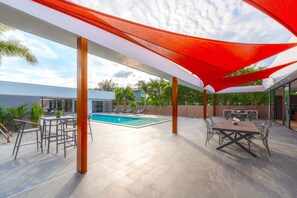 Relax by the pool in a semi- patio area with a dining table and lounge chairs.