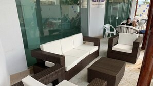 Un espace détente avec des meubles en osier et des coussins blancs, un mur en verre et un panneau dans le fond.