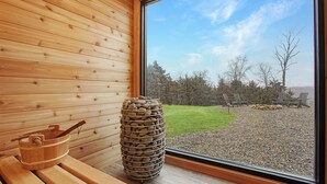 Una sauna con paredes de madera, un ventanal grande y piedras para el baño de calor.