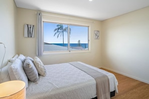 A bedroom with a large window, a bed with multiple pillows, and a view of the ocean. - Relaxing views over Seven Mile Beach (Lennox Head)