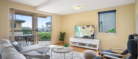 A living room with a sofa, armchairs, a coffee table, and a TV on a white stand.