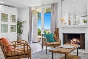 A room with a fireplace, wicker furniture, and a view of the outdoors. - Amazing Ocean Views-Walk Out Beach Access - Spacious living room area- North Coast Village G35 (Oceanside)
