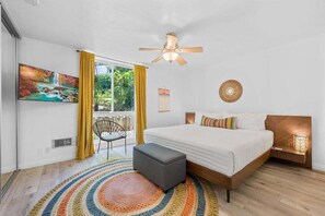 A bedroom with a bed, a ceiling fan, a window with curtains, a painting, and a rug.