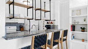 A modern kitchen with a granite countertop, black chairs with woven seats, and a white shelving unit with decorative items. - Amazing Ocean Views-Walk Out Beach Access - Spacious living room area- North Coast Village G35 (Oceanside)