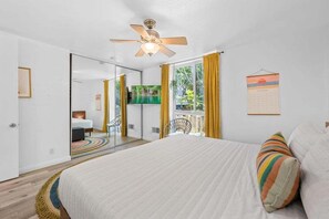 A bedroom with a bed, a ceiling fan, a TV, and a window with curtains.