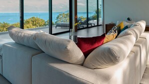 Un salon moderne doté d’une grande fenêtre donnant sur un balcon avec vue sur la mer.