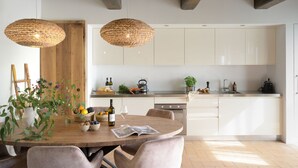 Een moderne keuken met witte kasten, een houten eettafel en twee gevlochten hanglampen.