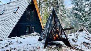 Una baita dal tetto spiovente e un braciere triangolare in una foresta innevata.