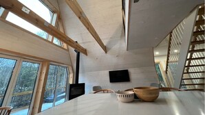 Un interno moderno con ampie finestre, un soffitto in legno e un'area pranzo con tavolo e sedie.