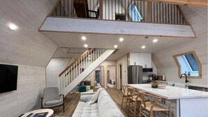 Un ambiente living in stile loft con soffitto alto, una scala, angolo cottura e zona salotto con divano e poltrone.