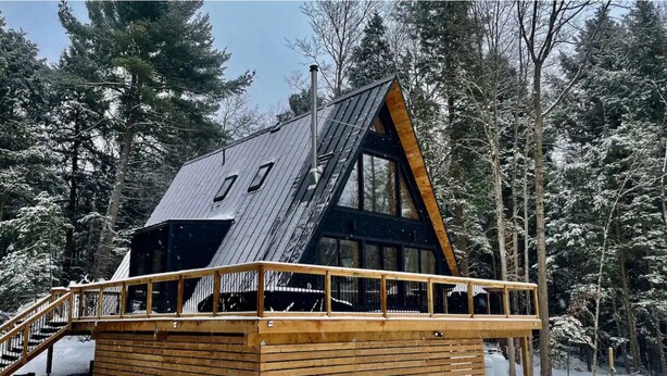 Una baita con tetto spiovente, ampie finestre e un patio in legno.