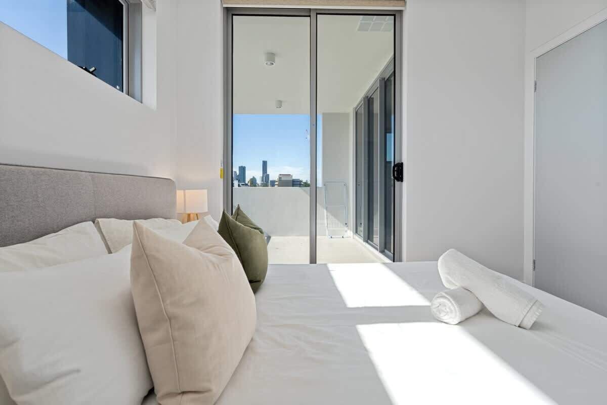 A modern hotel room with a large bed, a view of the city through a sliding door, and a balcony with a cityscape view.
