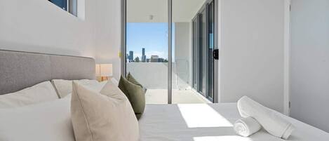 A modern hotel room with a large bed, a view of the city through a sliding door, and a balcony with a cityscape view.
