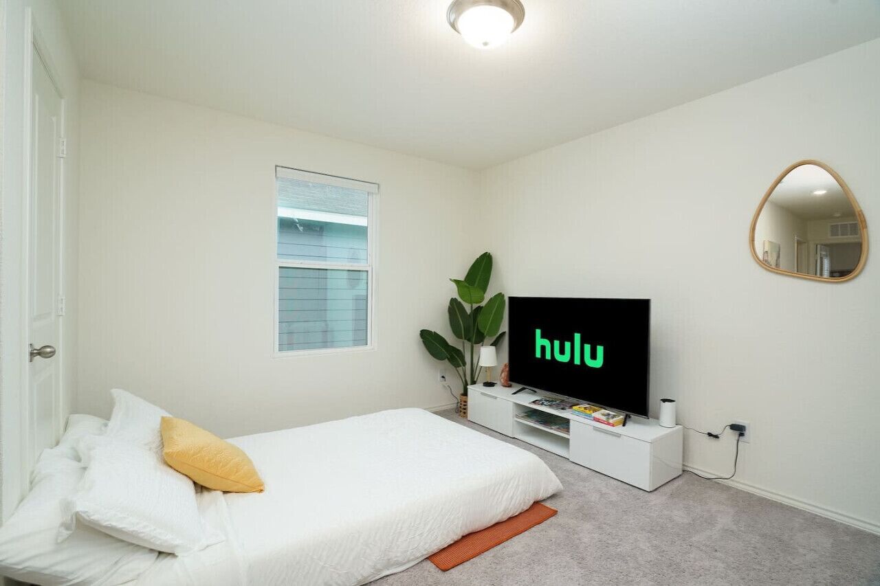 A bedroom with a bed, a TV displaying 'hulu', a window, and a mirror on the wall.