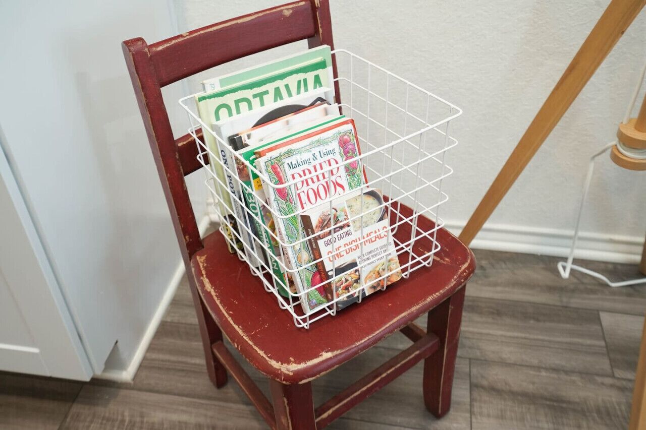 A wooden chair with a wire basket containing several books.