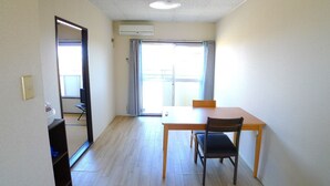 Una habitación con una mesa y sillas de madera, una lámpara en el techo, un equipo de aire acondicionado y un cristalero corredizo que da a un balcón.