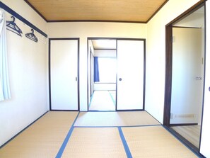 A room with tatami flooring, a sliding door, and a wall-mounted coat rack. - Silk Village (Itako)