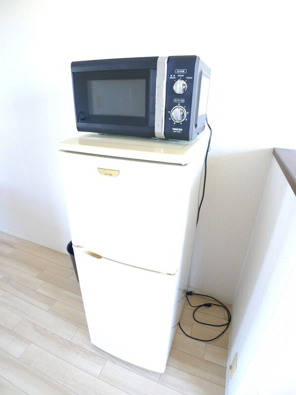 Un refrigerador compacto con un microondas encima, un cable de corriente en el suelo y una pared blanca al fondo.