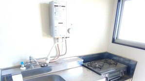 Una kitchenette compacta con un lavamanos, estufa y un pequeño cuadro eléctrico en la pared.