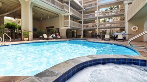 A swimming pool with lounge chairs and a hot tub area, surrounded by a multi-level building with balconies.