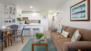 A modern living room with a brown sofa, a glass coffee table, and a dining area with patterned chairs and a glass table.