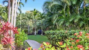 A tropical garden with a paved walkway, palm trees, and various flowering plants.