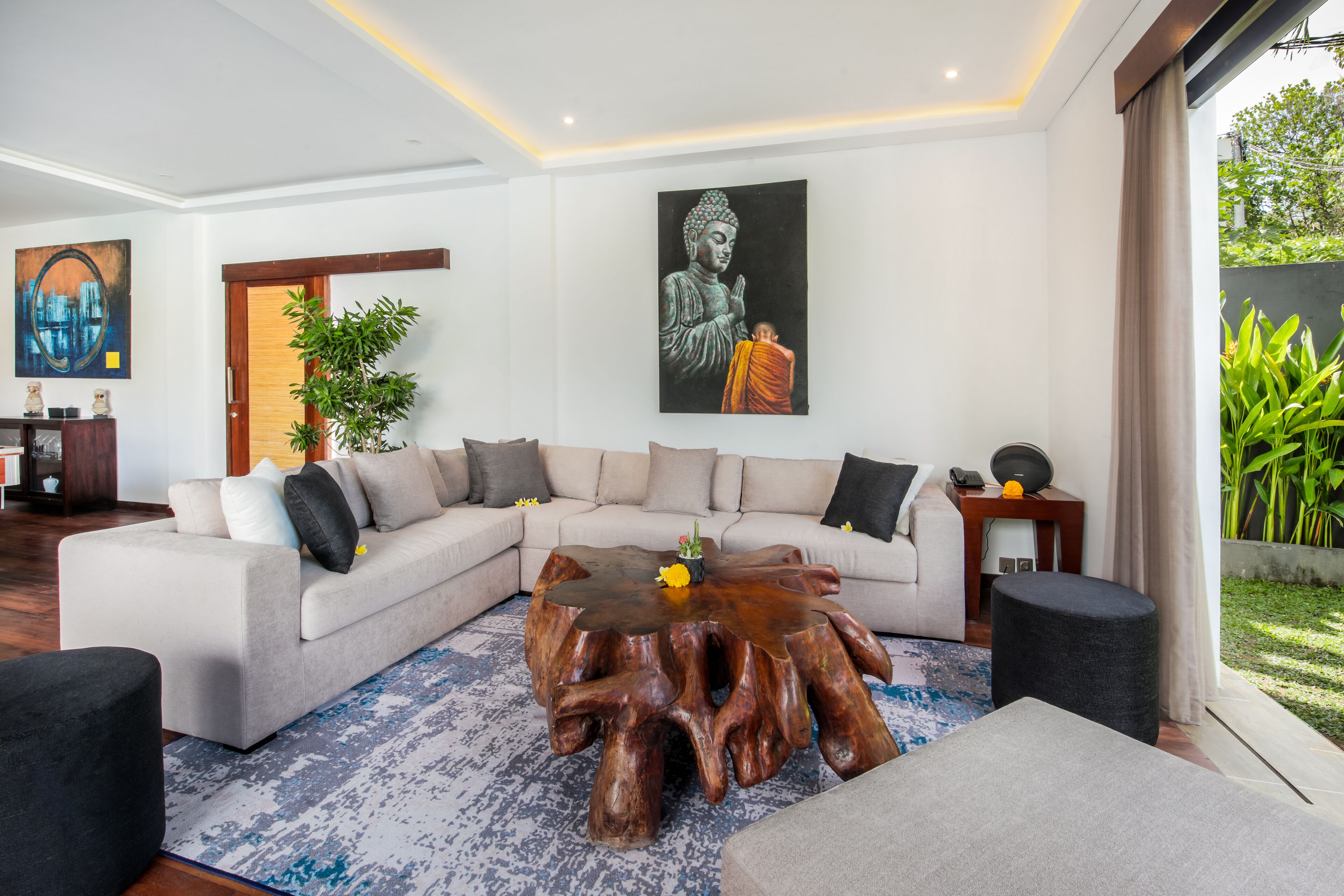 A modern living room with a sectional sofa, a round wooden coffee table, and a Buddha statue on the wall.