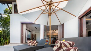 Et moderne udendørs opholdsområde med en stor parasol, to liggestole og et spisebord med drikkevarer.