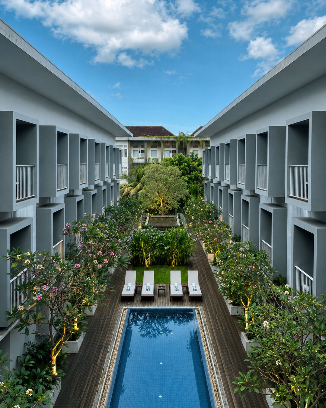 A modern hotel with a central pool, lounge chairs, and a garden view.