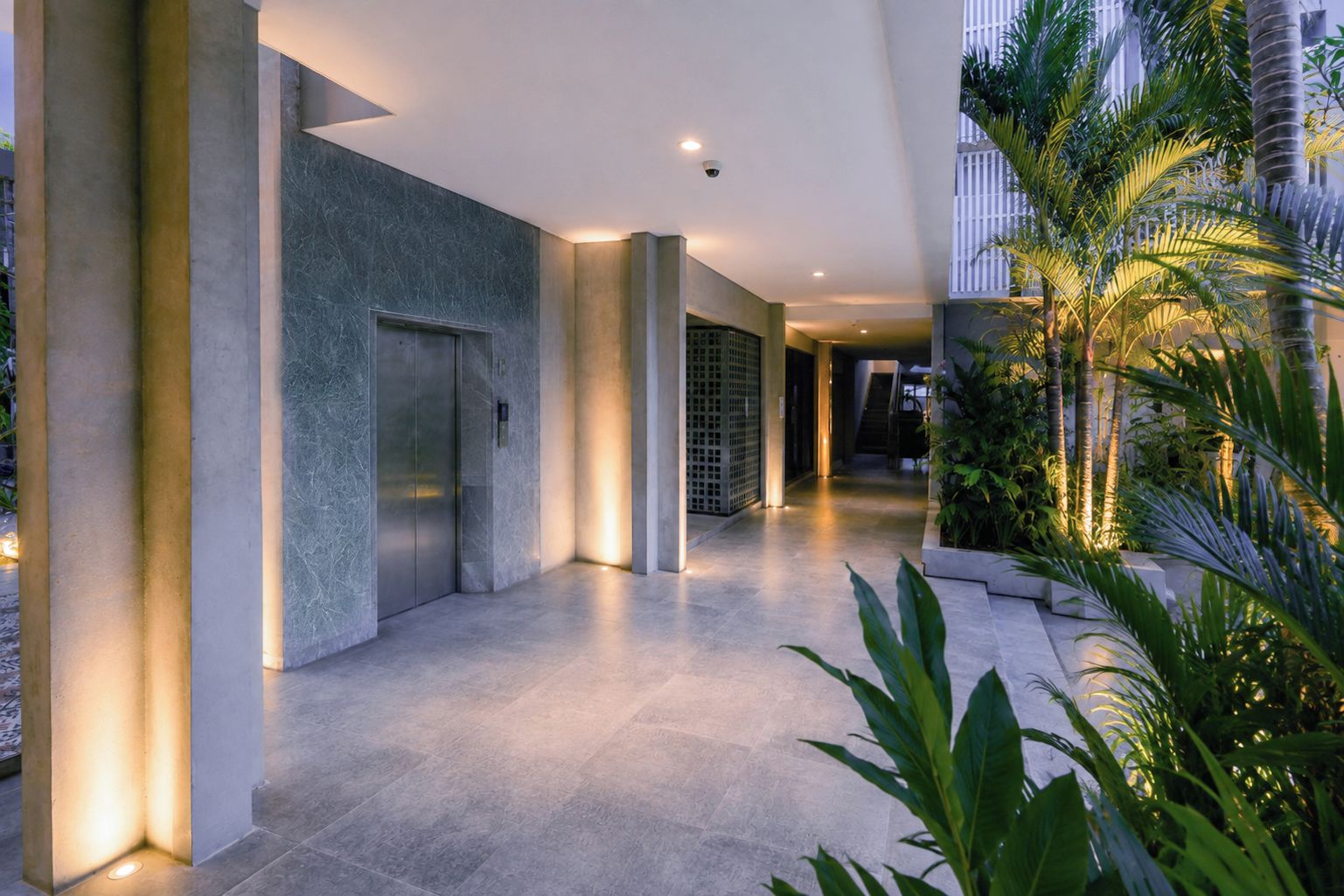 A modern hotel lobby with a marble floor, a reception desk, and a staircase leading to upper floors.