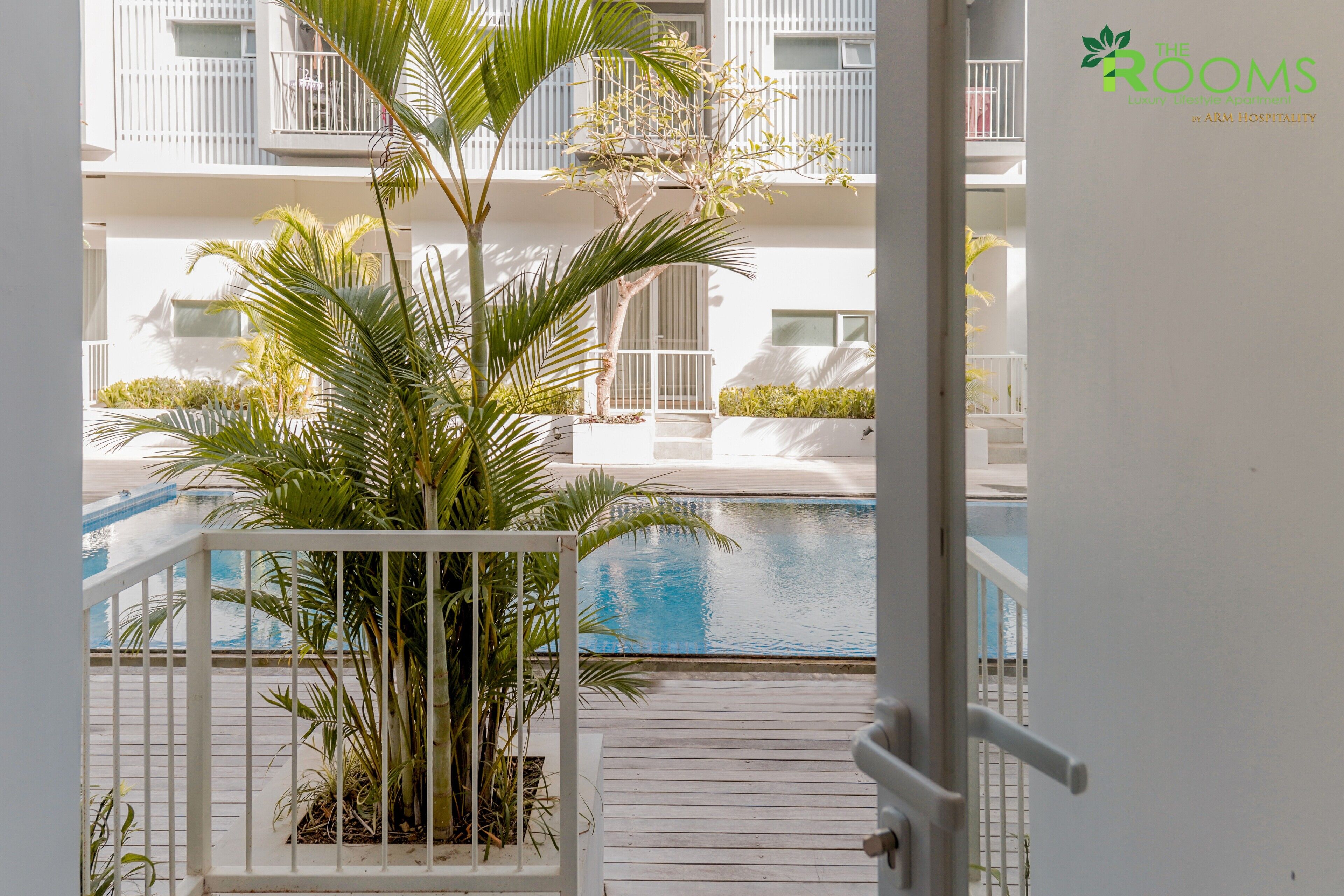 Vista de un área de piscina con una palmera y una barandilla blanca.