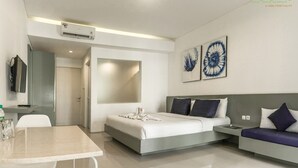 A modern hotel room with a bed, a sofa, a dining table, and artwork on the walls.