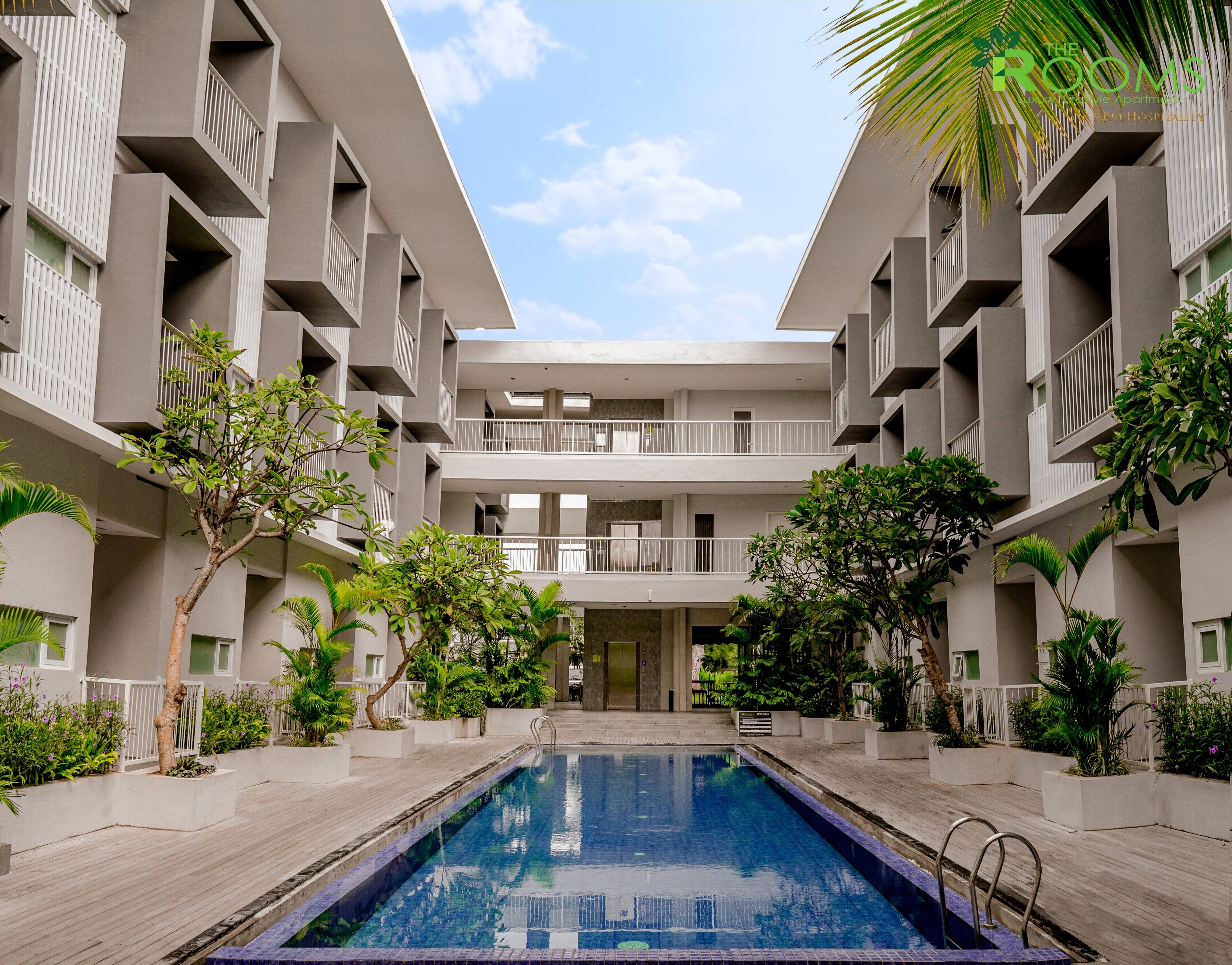 A modern hotel with a central pool, multiple balconies, and lush greenery.